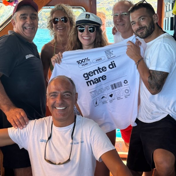 Group of six people on a boat, holding a 'gente di mare' shirt, smiling.