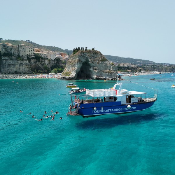 Boat on turquoise water near rocky coast, swimmers nearby.